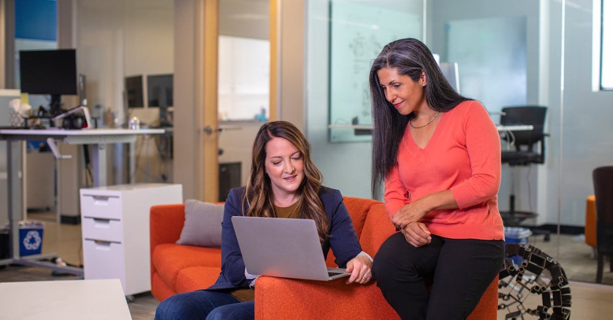 Two women working collaboratively on a laptop in a modern office environment, conveying teamwork and productivity.