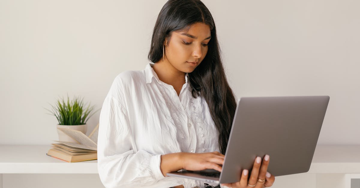 A young woman typing on a laptop while standing indoors, focused and professional.